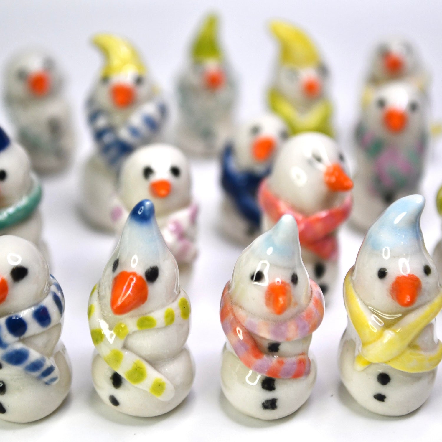 A group of small ceramic snowman figurines in various colorful winter outfits, arranged on a plain white background.